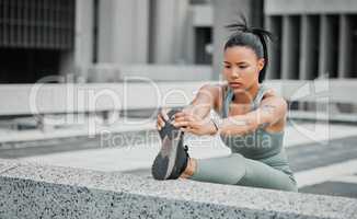 Young mixed race hispanic female athlete stretching her leg before a run outside in the city. Exercise is good for your health and wellbeing. Stretching is important to prevent injury