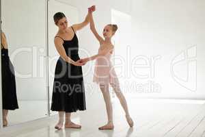 The principles of ballet focus on balance, coordination and poise. a young girl practicing ballet with her teacher in a dance studio.