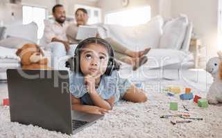 Closeup of a little cute girl using a laptop and wireless headphones while laying on the floor in the lounge. Hispanic girl using a wireless device to do her homework in the living room