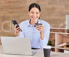 Beautiful young mixed race woman reading her credit card while using her phone and laptop to shop online while sitting in the office at work. Shopping has never been simpler or more convenient