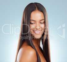 A hispanic brunette woman with long lush beautiful hair posing and smiling against a grey studio background. Mixed race female standing showing her beautiful healthy hair