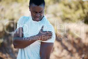 Active african american man holding his shoulder in pain while suffering from a sports injury during his workout in a nature environment. Man feeling discomfort in his arm while exercising outdoors