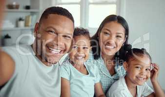 Photo of a cheerful father holding phone and taking selfie or recording funny video with his family. Happy mixed race family with two children and parents posing together for a family picture on a mobile phone