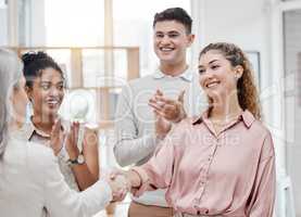 Happy businesswomen shaking hands while their colleagues clap hands in support in a meeting at work. Business professionals greeting and making deals with each other. Boss hiring an employee