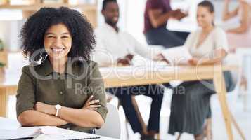 Happy mixed race businesswoman sitting with her arms crossed in an office at work. Confident female businessperson with a curly afro smiling while sitting at a table at work