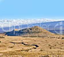 Copy space with a volcano crater on a cloudy blue horizon. Empty barren nature scene of dry grass fields over a mountain and a hiking trail. High angle background of Mauna Loa in Hawaii
