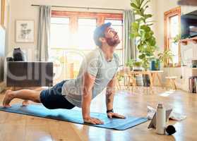 One fit young caucasian man doing cobra push up bodyweight exercise while training with online tutorial on digital tablet at home. Focused guy challenging himself to gain muscle, core strength and increase endurance during yoga workout