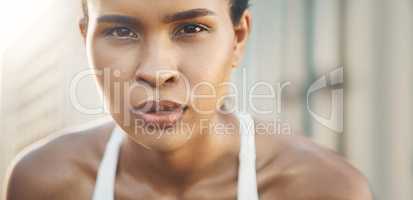 Closeup portrait of one fit young hispanic woman taking a rest break to catch her breath after a run or jog in an urban setting outdoors. Female athlete looking tired but determined after intense cardio exercise