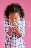 A pretty little mixed race girl with curly hair blowing on coins in her hands against a pink copyspace background in a studio. African child looking excited about her savings
