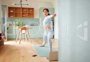 Beautiful young mixed race woman using a laptop to follow an online class while practicing yoga at home. Hispanic female exercising her body and mind, finding inner peace, balance and clarity