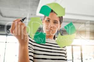 Young focused mixed race businesswoman drawing a recycle symbol on a glass window in an office at work. One serious hispanic businessperson drawing a sign for awareness to recycling