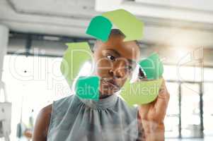 Young focused african american businesswoman drawing a recycle symbol on a glass window in an office at work. One serious black female businessperson designing a sign for awareness to recycling