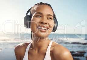 Young mixed race female athlete looking happy and smiling while wearing headphones and listening to music while out for a run along the promenade. Exercise for a healthier mind and body