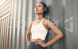 One fit young hispanic woman wearing headphones and taking a rest break to catch her breath after a run or jog in an urban setting outdoors. Female athlete looking tired after intense cardio exercise
