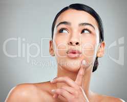 A beautiful young mixed race woman with glowing skin posing against grey copyspace background. Hispanic woman with natural looking eyelash extensions smiling while feeling her smooth skin in a studio