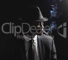 A young African american male looking serious while smoking a cigarette against a black background. African looking like hes deep in thought wearing a black formal suit and a hat with isolated cigarette smoke. The choices we make determine our future