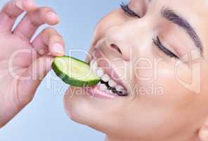A beautiful mixed race woman holding cucumber slice. Hispanic model promoting the skin benefits of a healthy diet against a blue copyspace background