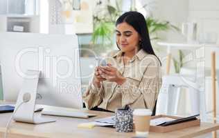 One beautiful young mixed race businesswoman using her smartphone during a lunch break in the office at work. Confident and successful female entrepreneur of indian ethnicity working on a cellphone in her workplace looking motivated and happy.