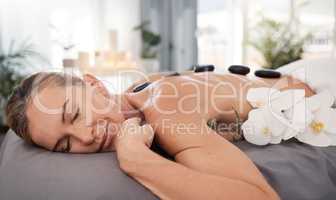 Hot stones calm the psyche and absorb toxins. Shot of a mature woman enjoying a relaxing hot stone massage at a spa.