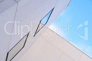 Angled view of tall building exterior on a sunny day. Concept of modern white housing with reflective windows against a blue sky. Abstract background of architecture for copy space outside