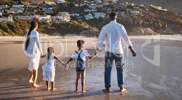 Rear view of carefree young african american family with two children holding hands and looking at the view while getting their feet wet enjoying family vacation by the beach
