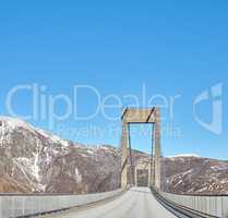 Empty road in the mountains against a blue sky with copy space. Deserted highway crossing in the cold snowy and grey hills around Bodo in Norway. Polar landscape of old bridge over a ravine or river