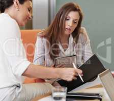 Two business women with laptops and notepads having a meeting in their office. Two business women with laptops and notepads having a meeting in their office.