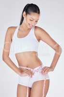 Achieving her weightloss goals. Studio shot of an attractive young woman using a measuring tape against a grey background.