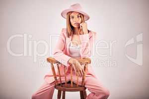 Portrait of serious young mixed race female posing in trendy fashionable clothing, sitting on a chair in a grey studio background. Hispanic woman showing the latest fashion collection with cool style