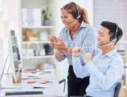 Two happy young diverse call centre telemarketing agents clapping and cheering with joy while working together in an office. Excited african american and asian assistants celebrating successful sales and reaching targets to win