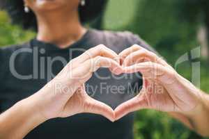 Closeup of a person showing a heart gesture outside in nature. A female expressing love, care and peace using heart shaped gesture. A person showing the heart with their hands