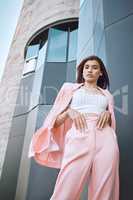 Portrait of a young trendy and confident mixed race woman looking stylish while posing and chilling time in the city. Fashionable hispanic woman wearing pink clothes and standing outside downtown