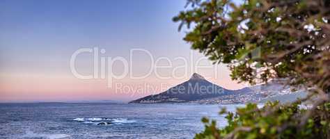 Wide angle of a mountain on a coastline at sunset in South Africa. Scenic nature landscape of Lions Head at dawn near a calm peaceful sea against a blue horizon with copy space in Cape Town