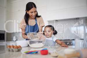 Single mother teaching daughter baking skills and bonding together in home kitchen. Cute little girl learning cooking with her smiling mom. Happy parent showing curious child how to sieve flour