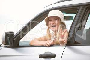 One beautiful blonde caucasian woman gesturing peace while enjoying a roadtrip. An attractive young female leaning out of the passenger window of a car while taking a drive. Enjoying the open road