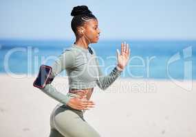 Fit and active African American woman listening to music through earphones and running alone on a beach for workout. Focused black athlete training, exercising and using a cellphone to track progress