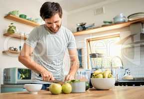 One fit young caucasian man cutting ingredients with knife to make healthy green detox smoothie while wearing earphones in kitchen at home. Guy having fresh fruit juice to cleanse and provide energy for training. Wholesome drink with vitamins and nutrient