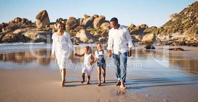 Happy young african american family with two children holding hands and having fun while walking along beach. Loving parents enjoying vacation with cheerful little daughter and son