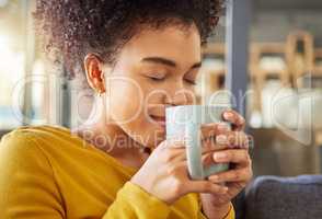 Young happy mixed race woman holding and drinking a cup of coffee at home. One cozy hispanic female smelling and enjoying a cup of tea while relaxing at home