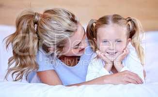 Happy caucasian mother and daughter lying on a bed at home. Cheerful woman with cute little girl enjoying a cosy and lazy relaxing day together. Loving parent bonding and sharing quality time with kid