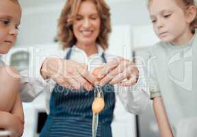 First we start by cracking a few eggs. Closeup shot of a grandmother cracking an egg while baking with her two granddaughters at home.