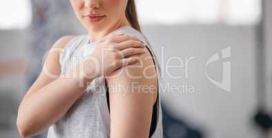 Closeup of one caucasian woman holding her sore shoulder while exercising in a gym. Female athlete suffering with painful arm injury from fractured joint and inflamed muscles during workout. Struggling with stiff body cramps causing discomfort and strain