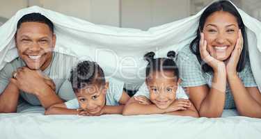 Portrait of happy family with two children lying under duvet smiling and looking at camera. Little girl and boy lying in bed with their parents bonding and having fun