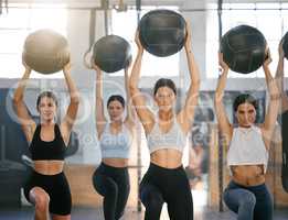 Diverse group of active young people doing overhead medicine ball lunge exercises while training together in a gym. Focused athletes challenging themselves by holding weighted equipment to build muscle and endurance during a workout in a fitness class