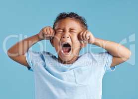 Unhappy little hispanic boy looking upset and crying while rubbing his eyes against a blue studio background. Unhappy preschooler kid bawling his eyes out