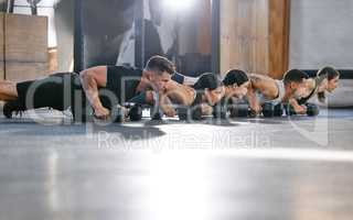 Diverse group of active young people doing push up exercises with dumbbells while training together in a gym. Focused athletes doing press ups with heavy weights to build muscle and endurance during a workout in a fitness class