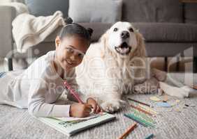 Sweet little mixed race child doing her homework while lying on the living room carpet with her puppy. Child colouring while bonding with her emotional support rescue dog