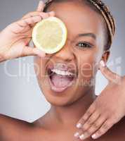 When life gives you lemons, have a spa day. Studio shot of an attractive young woman holding a sliced lemon against a grey background.