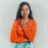One mixed race woman isolated against grey studio background with copyspace. Young hispanic standing alone and thinking. Contemplative model with finger on chin planning and coming up with an idea