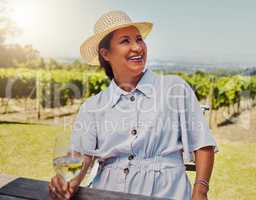 One smiling mature mixed race woman enjoying a wine tasting day on a farm. Happy hispanic woman wearing a hat while sitting alone on a vineyard. Woman holding a glass of white wine during the weekend